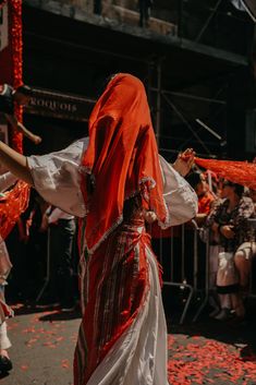 a woman in an orange and white dress walking down the street with her arms outstretched