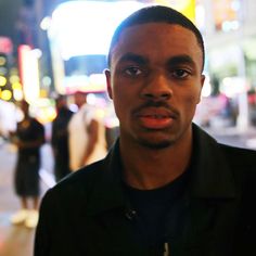 a man standing in front of a city street at night with buildings and people behind him