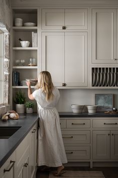 a woman standing in a kitchen next to a counter with plates and bowls on it