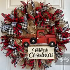 a christmas wreath with a red truck and plaid ribbon hanging on the front door to say merry christmas