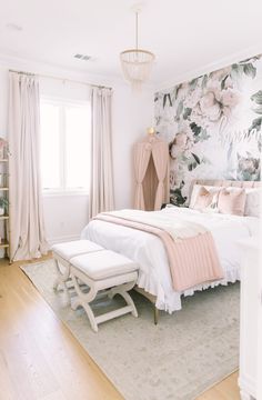 a white bed sitting next to a window in a bedroom under a chandelier