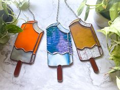 three popsicle shaped stained glass pendants hanging from a chain on a marble surface