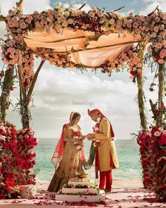 a man and woman standing in front of a wedding arch with flowers on the beach