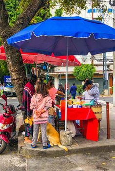 people standing under an umbrella selling food on the side of the road with their dogs