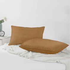 two brown pillows sitting on top of a bed next to a white nightstand with a clock