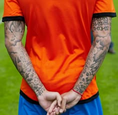 a man with tattoos on his arm holding hands in front of the camera while wearing an orange shirt and blue shorts