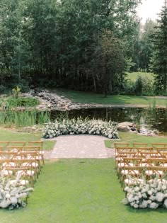 an outdoor ceremony set up with chairs and flowers on the grass, near a pond