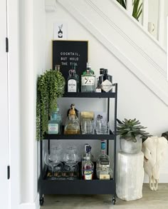 a shelf with liquor bottles and glasses on it in front of a stair case next to a potted plant