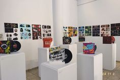 several records are on pedestals in an art gallery, with various pictures hanging on the wall behind them