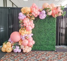 an arrangement of balloons and greenery on a carpeted floor in front of a backdrop