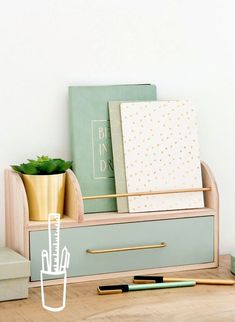 an assortment of stationery items sitting on top of a wooden desk next to a plant