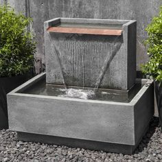 an outdoor fountain with water coming out of it and plants in the back ground next to it