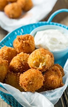 some fried food is in a blue basket on a wooden table next to dip and sour cream