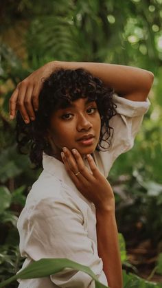 a woman with curly hair is posing for a photo in the woods wearing a white shirt