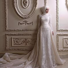 a woman in a white wedding dress standing next to a wall with ornate paintings on it