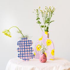 two vases with flowers are sitting on a table next to each other, one is painted pink and the other is blue