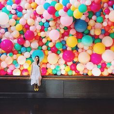 a woman standing in front of a large amount of balloons on the wall behind her