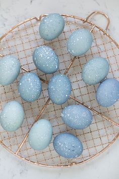 blue and white speckled eggs sitting on a gold wire rack in front of a marble counter top