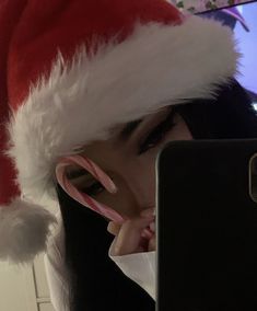 a woman wearing a santa hat looking at her cell phone with candy cane in front of her