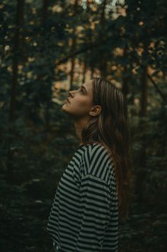 a woman standing in the woods looking up into the sky with her head tilted back