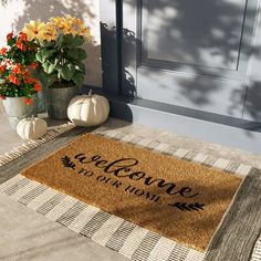 a welcome mat is on the front porch next to potted flowers and pumpkins