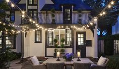 an outdoor dining area with lights strung over the table and chairs, in front of a house