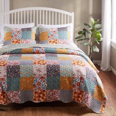 a bed with a colorful quilt on top of it next to a white headboard