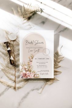 the wedding stationery is laid out on a marble surface with flowers and feathers around it