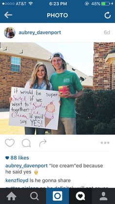 two people standing in front of a house holding a sign