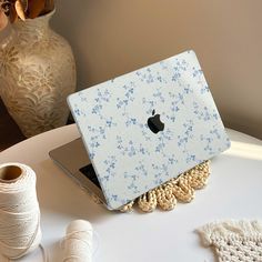 an apple laptop computer sitting on top of a white table next to yarn and spools of thread