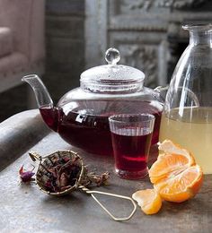 tea and orange slices sit on a table next to a glass teapot with a strainer