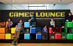 a group of people sitting on top of colorful cubes in front of a sign that says game lounge