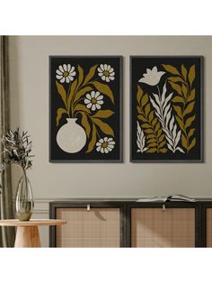 two black and gold paintings on the wall above a table with flowers in vases