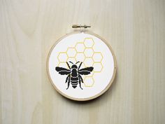 a cross stitch bee with honeycombs on it's back is hanging from a wooden hoop