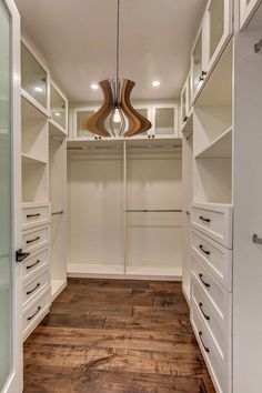 an empty walk - in closet with white cabinets and drawers on the wall, along with wood flooring