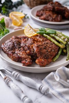 two plates with meat, asparagus and lemon wedges on them next to silverware