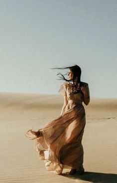 a woman in a long dress is walking through the desert with her hair blowing in the wind