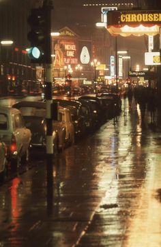 cars are parked on the side of the road in the rain as people walk down the street