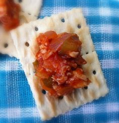 some crackers with food on them sitting on a blue and white checkered table cloth