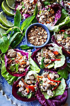 several lettuce wraps with meat and vegetables on a blue plate next to lime wedges