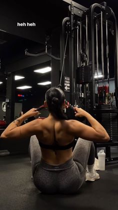 a woman squats on the ground in front of a gym machine and holds her hands behind her head