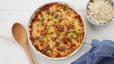 a casserole dish with meat, cheese and rice next to a wooden spoon