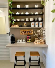 two wooden stools sitting in front of a counter with coffee cups and teapots on it