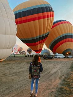 a woman is standing in the dirt with several hot air balloons flying above her head