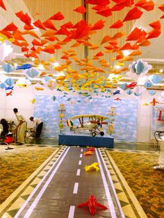 an indoor area decorated with orange, blue and white paper cranes hanging from the ceiling