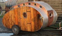 a wooden barrel sitting on top of a trailer in front of a building with metal pipes