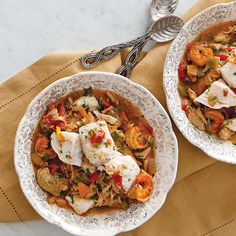 two white bowls filled with food on top of a brown napkin next to silver spoons