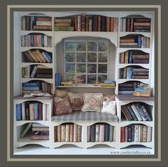 a bookshelf filled with lots of books next to a window covered in pillows