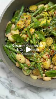 a pan filled with green beans and vegetables on top of a marble countertop next to a