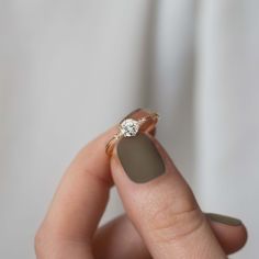 a woman's hand holding a ring with a diamond on it and a white background